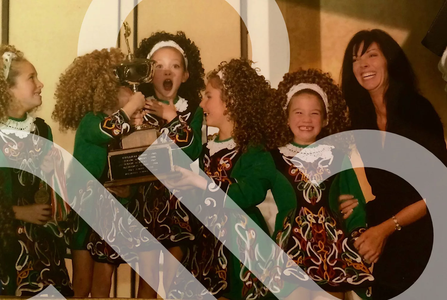 An image from IDTANA's history with several girls in ceili dresses screaming while holding a perpetual trophy. The IDTANA logo is interwoven through.
