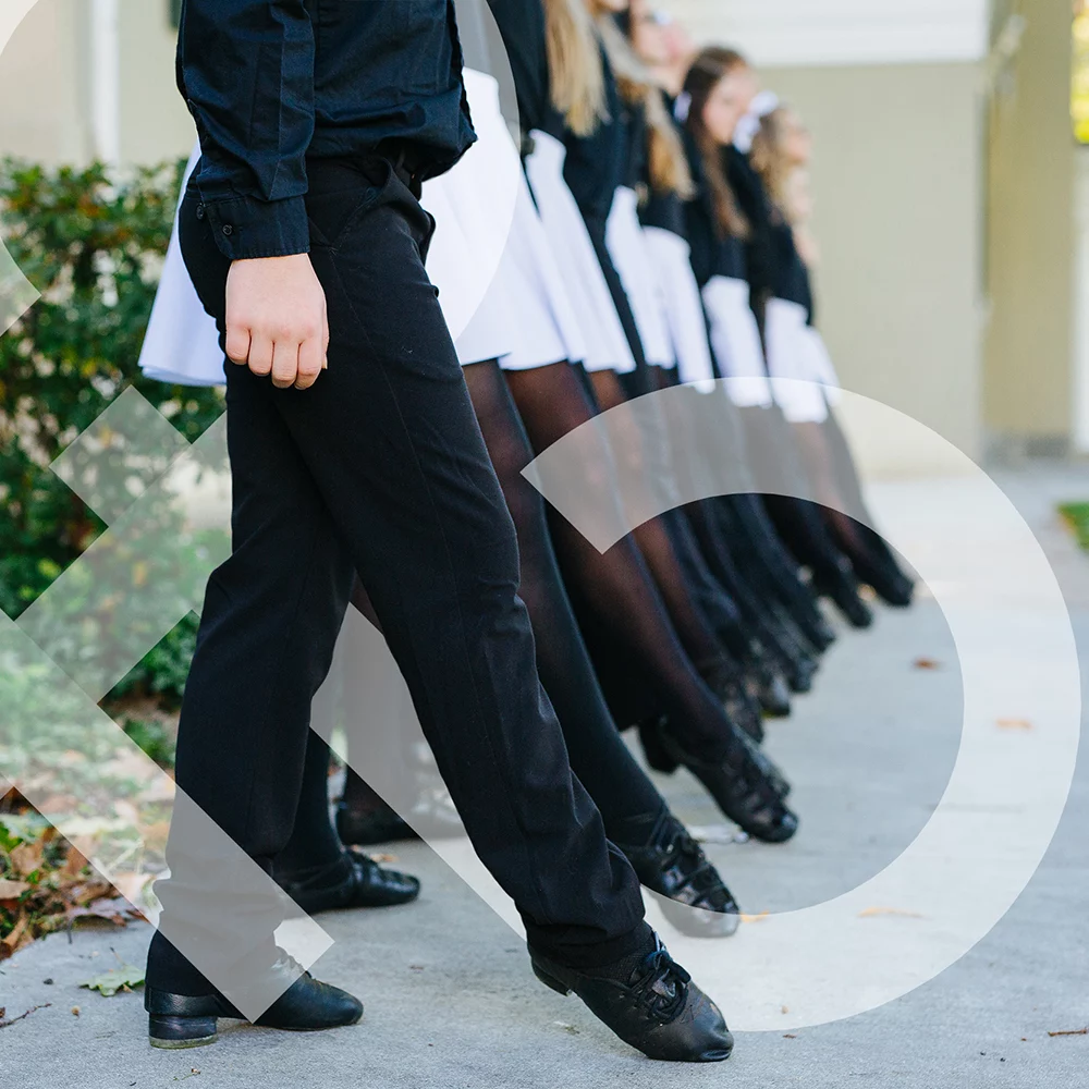 A line of Irish dancers pointing their toes and wearing soft shoes. The girls are wearing black tights and the boy is