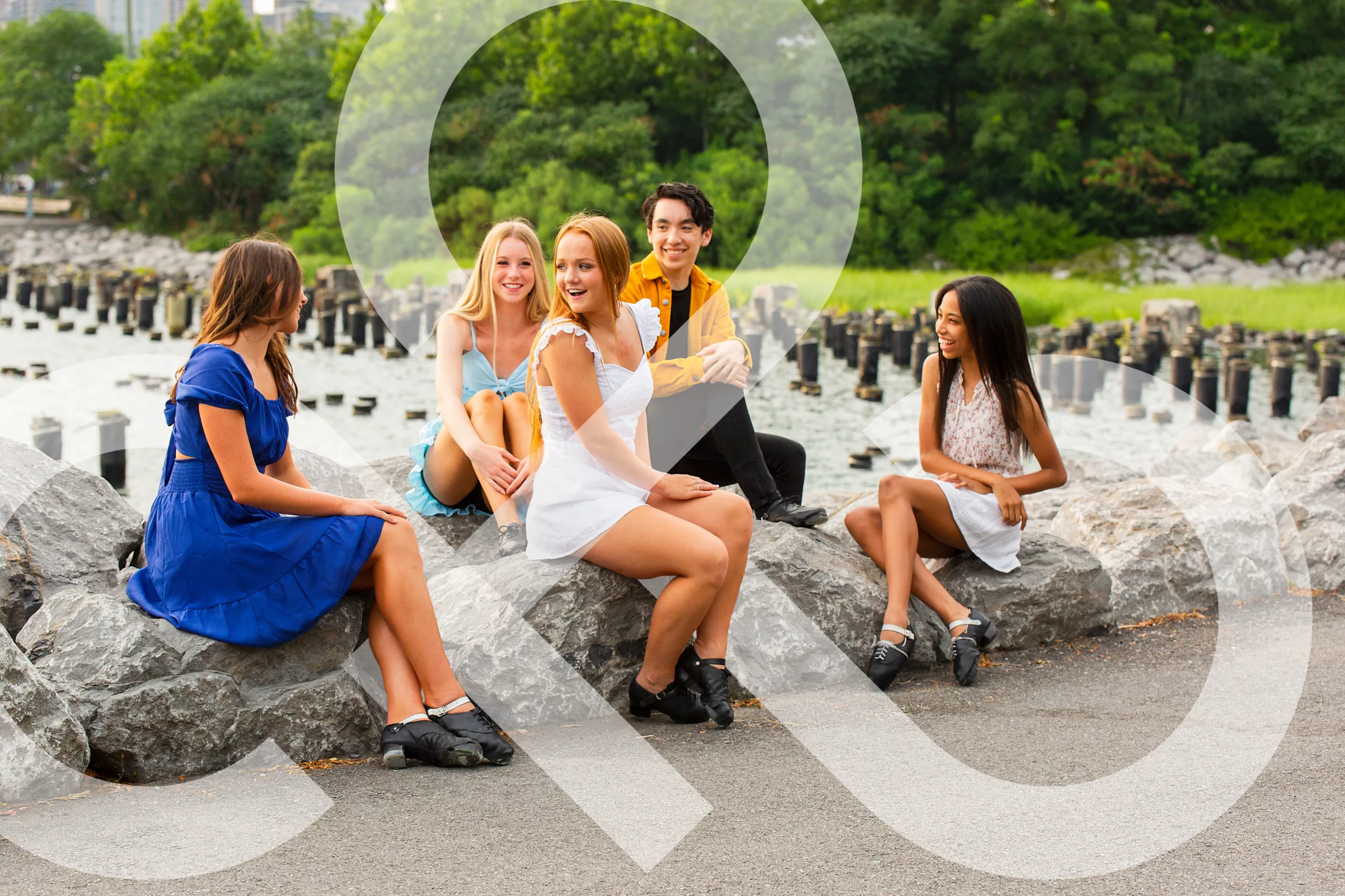 A picture of five teenagers, four girls and one boy, sitting on rocks by the water, wearing Irish dance shoes. The IDTANA logo is woven throughout.